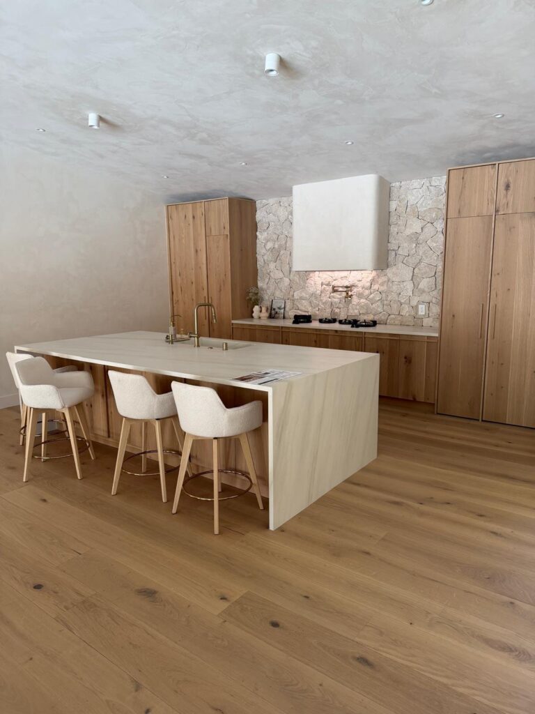 Organic modern kitchen with white oak cabinets, a natural stone backsplash, and a quartzite waterfall island