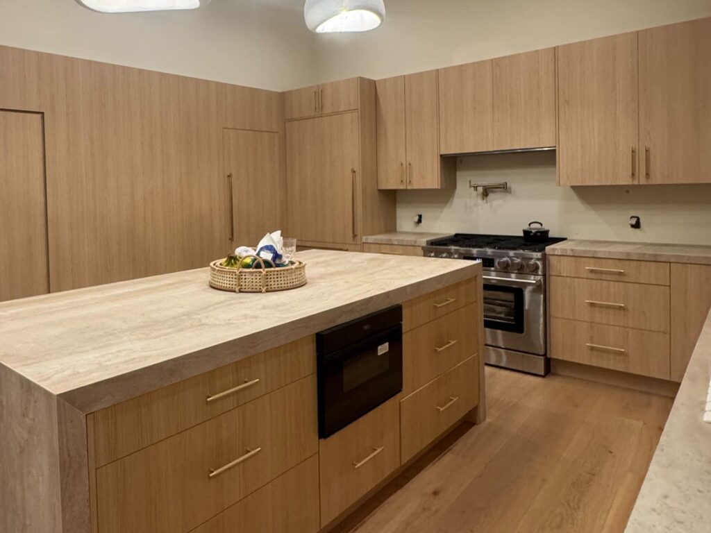 White oak kitchen with a travertine island and a stainless steel range
